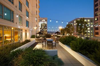 A rooftop patio with a table and chairs is illuminated by string lights.